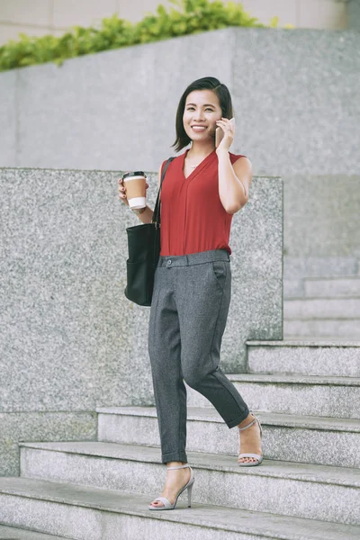 Asian young businesswoman walking down the stairs in the city and talking on mobile phone with smile