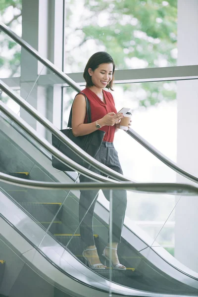 現代的なオフィスビルの掘削機に立っている間に彼女の携帯電話と笑顔を使用して若い実業家 — ストック写真