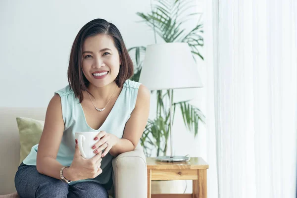 年轻的亚洲妇女坐在一张咖啡和微笑在家里的相机的肖像 — 图库照片