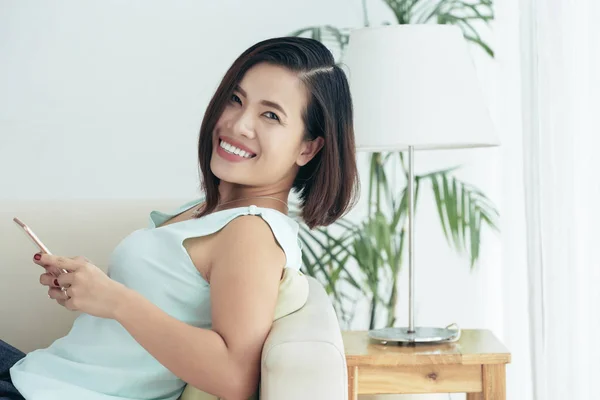 전화를 사용하여 집에서 소파에 미소로 카메라를 보고있는 아시아 행복한 소녀의 — 스톡 사진
