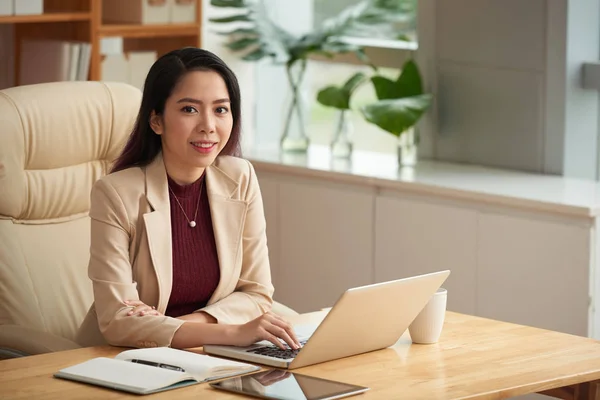 漂亮的微笑的亚洲女企业家在她的桌子上工作笔记本电脑的肖像 — 图库照片