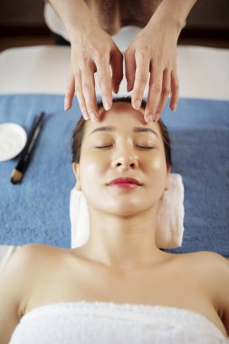 Güzel genç Asyalı hastaya yağlar ile nazik yüz masajı veren Beautician 