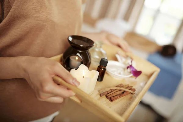 Spa salon worker carrying tray with aroma lamp, candes and essential oils