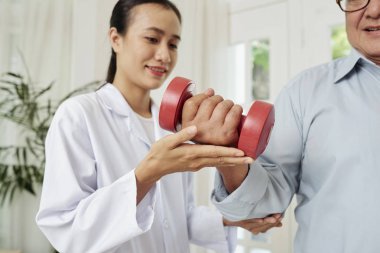 Beyaz ceketli Asyalı kadın doktor ameliyattan sonra rehabilite için yaşlı adam yardım, onlar hastanede dumbbell ile eğitim