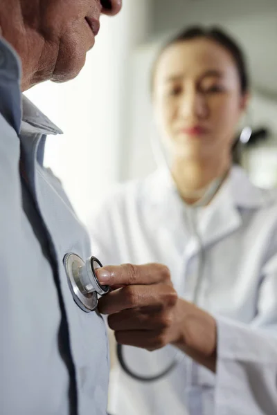 Close-up of senior man standing while female doctor listening to his heart at the office