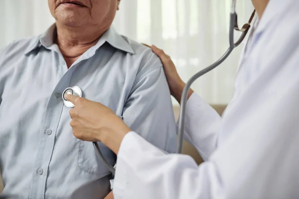 病院訪問中に先輩男性の呼吸を聞く白いコートを着た女性医師のクローズアップ — ストック写真