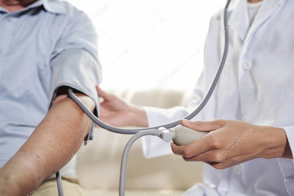 Close-up of female doctor examining her senior patient while coming to visit him at home
