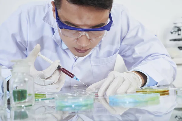 年轻科学家穿着实验室外套 防护眼镜和手套 带着注射器样本在实验室做科学实验 — 图库照片