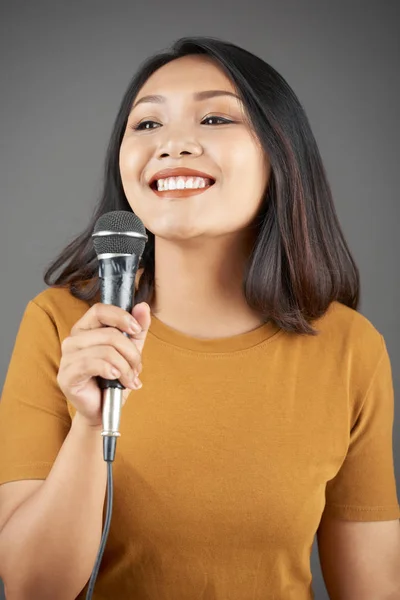 Happy young Asian woman with microphone singing song or telling story on microphone