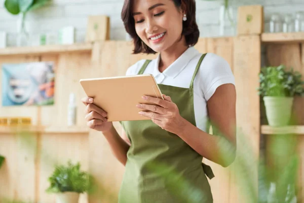 微笑的亚洲妇女浏览数字平板电脑 并穿着绿色围裙在家里 — 图库照片