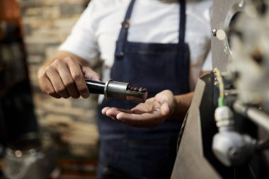 Apronda çalışan işçinin kavrulmuş kahve çekirdeklerini incelediği ve kahve fabrikasında dururken kalitelerini kontrol ettiği