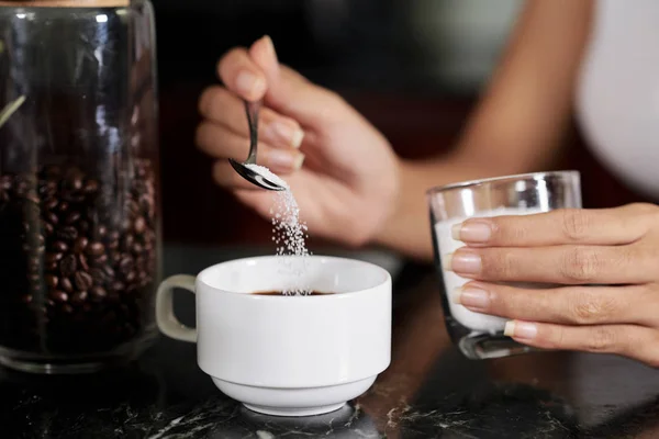 Close-up of woman putting a spoonful of sugar in a cup and making coffee drink for breakfast in the morning