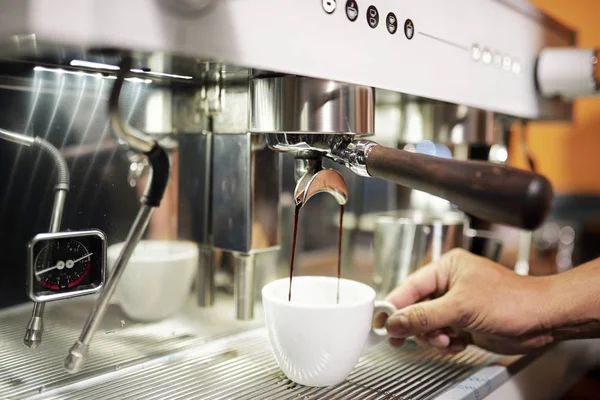 コーヒーマシンから流れるコーヒーの下にカップを入れて レストランでゲストのためにそれを準備するバリスタのクローズアップ — ストック写真