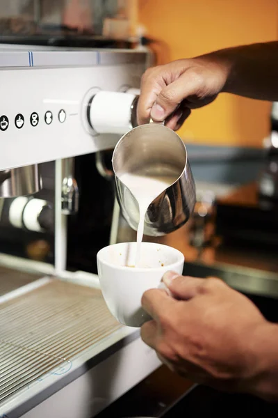コーヒーマシンで作られたコーヒードリンクとカフェでこのカップにジャグからミルクを注ぐ男性バリスタ保持カップのクローズアップ — ストック写真