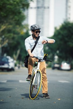 Neşeli genç adam bisiklet üzerinde oturan ve onun gözetiminde zaman kontrol