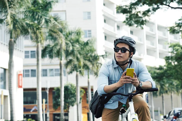 在街上骑车时戴着太阳镜和头盔的智能手机的男人 — 图库照片