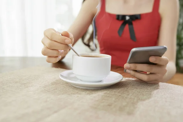 坐在桌旁喝杯咖啡 用手机在线交流的女人的特写镜头 — 图库照片