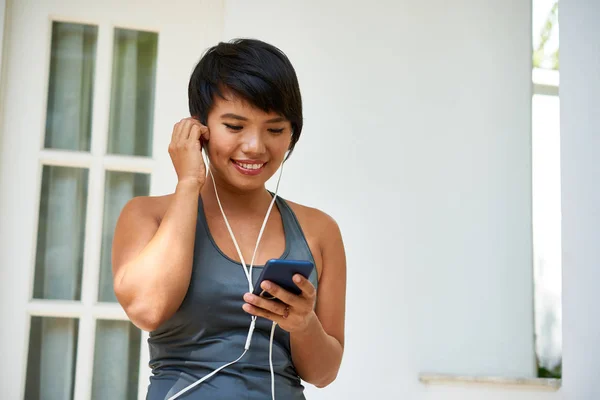 微笑的瑜伽士戴着耳机 在她的智能手机上选择音乐 — 图库照片