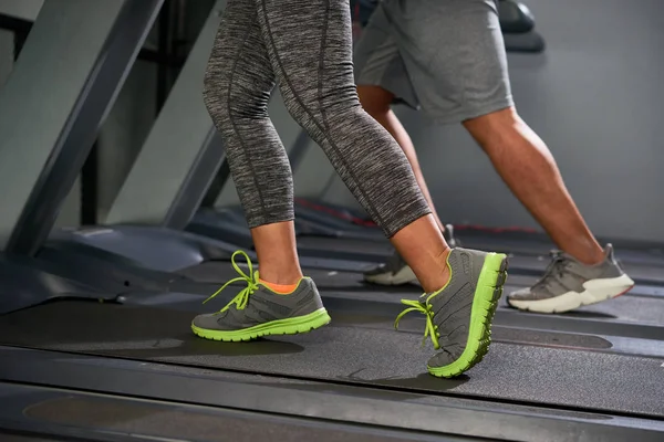 Legs of sporty active people running on treadmills in gym, cropped image