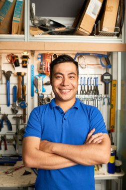Yakışıklı Asyalı adam kolları geçti ve arka planda araçları ve aletleri ile kameraya gülümseyen ayakta Portresi
