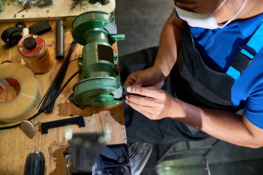 Apron ve koruyucu maskeli zanaatkar masada otururken ve atölyede detaylarla makinede çalışarak