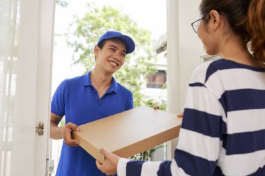 Mavi üniformalı neşeli teslimatçı müşteriye bir kutu sıcak lezzetli pizza veriyor.