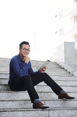 Elinde tablet bilgisayar ile Mutlu yakışıklı genç girişimci adımlar üzerinde oturan ve kamera bakıyor 