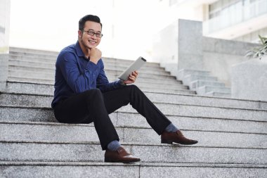 Hırslı genç Asyalı iş yöneticisi dijital tablet ile adımlar üzerinde dinlenme