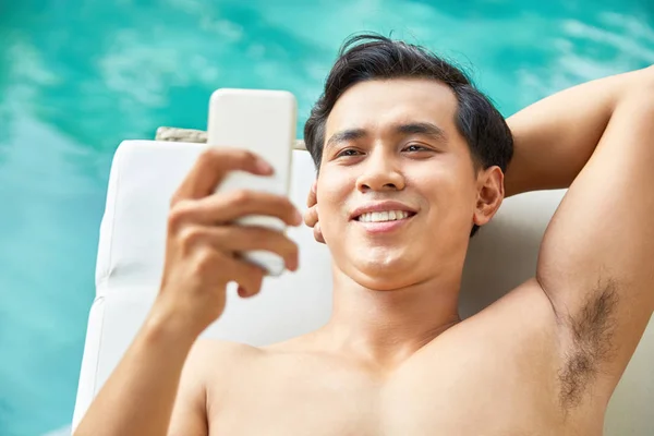 Joven Hombre Asiático Sonriente Tumbado Una Tumbona Usando Teléfono Móvil —  Fotos de Stock