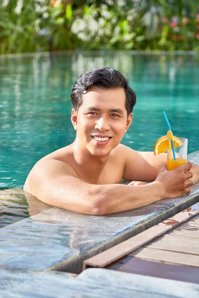 プールサイドでカクテルを飲み 屋外のカメラで微笑むハンサムなアジア人男性の肖像画 — ストック写真