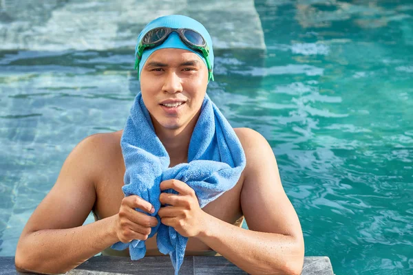 亚洲年轻运动员戴着泳帽 戴着护目镜站在水里 肩上扛着毛巾 对着镜头微笑 — 图库照片