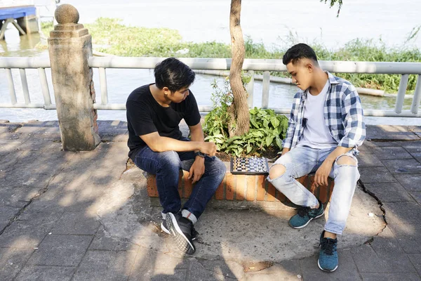 Beyinlerini eğiten iki Asyalı genç, satranç tahtasıyla oturup dışarıda satranç oynuyorlar. 