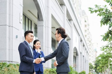 Asyalı genç işadamı gülümseyerek ve ofis binası yakınında yardımcısı açık havada meslektaşı tebrik 