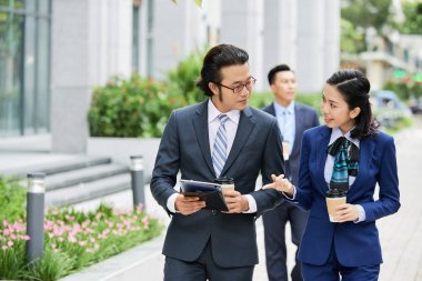 Asyalı iş çift kahve içme ve arka planda işadamı ile şehirde yürürken dijital tablet online iş tartışıyor 