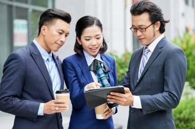 Dijital tablet tutan iki işadamı, iş kadını ise dijital tabletteki online çalışmaları açık havada anlatıyor