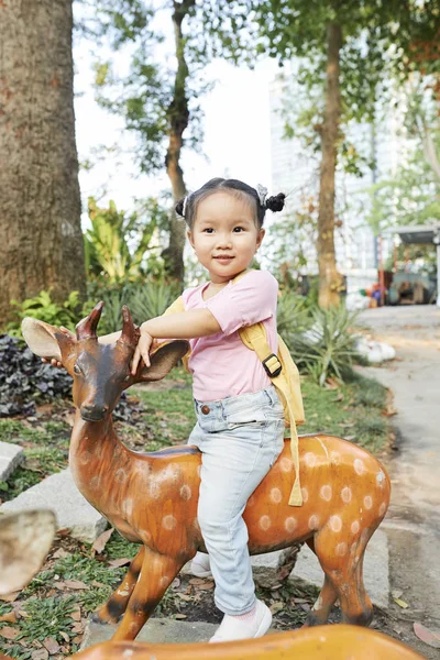 公園で木製の鹿の上に座っているかわいいベトナムの女の子の肖像画 — ストック写真