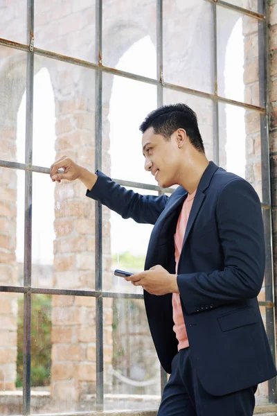 Šťastný Mladý Asijský Podnikatel Smartphone Který Opírá Okno Kanceláře Dívá — Stock fotografie