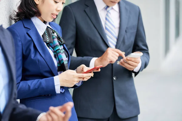 Açık havada cep telefonlarını kullanarak çevrimiçi olarak ayakta duran ve iletişim kuran iş adamlarının yakın çekim