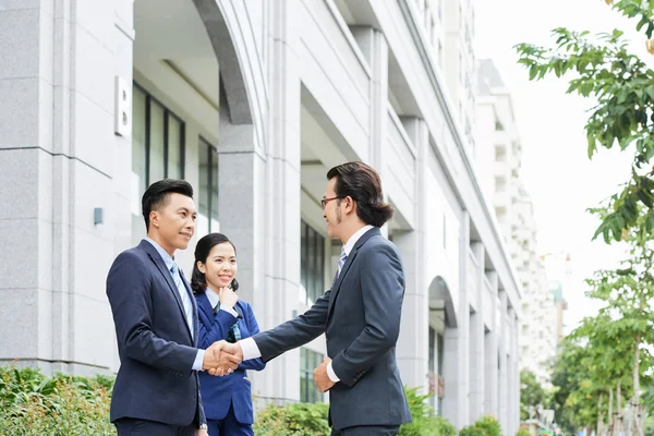 Asyalı genç işadamı gülümseyerek ve ofis binası yakınında yardımcısı açık havada meslektaşı tebrik 