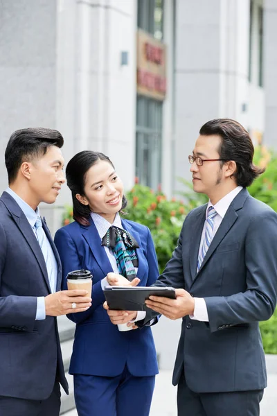 Dijital tablet kullanarak şehirde açık havada duran ve ekip içinde çalışmalarını tartışan üç ofis çalışanı grubu 