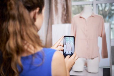 Cep telefonu tutan ve manken asılı bitmiş bluz fotoğraf çekmek ve onun müşterigöndermek terzi Arka görünümü