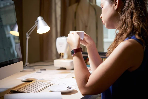 年轻疲惫的女人坐在工作场所的电脑显示器前 一边喝着咖啡 一边在办公室喝咖啡 — 图库照片