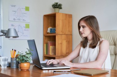 Ciddi ofis yöneticisi ofiste işyerinde oturan ve dizüstü bilgisayar kullanarak online çalışma