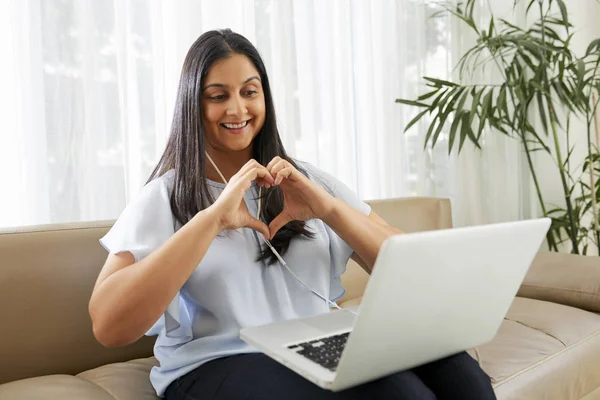 Happy woman making heart shape with her hands when video calling with laptop