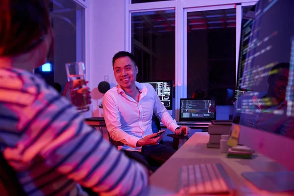 アジアの若いビジネスマンが椅子に座り オフィスで夜の仕事中に水を飲みながら若い女性と話をする笑顔 — ストック写真