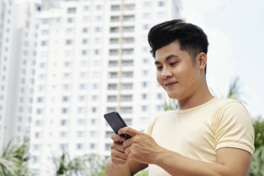 Gülümseyen genç Asyalı adamın telefonunda metin mesajları okuma portresi