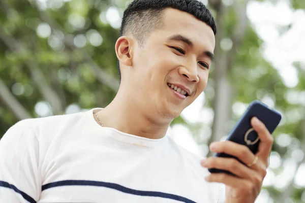 屋外に立っているアジアの若い男性に笑顔のテキストメッセージの肖像画 — ストック写真