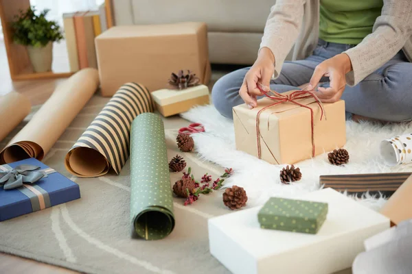 床に座って カラフルな紙とひもでクリスマスプレゼントを飾る女性の作物ショット — ストック写真