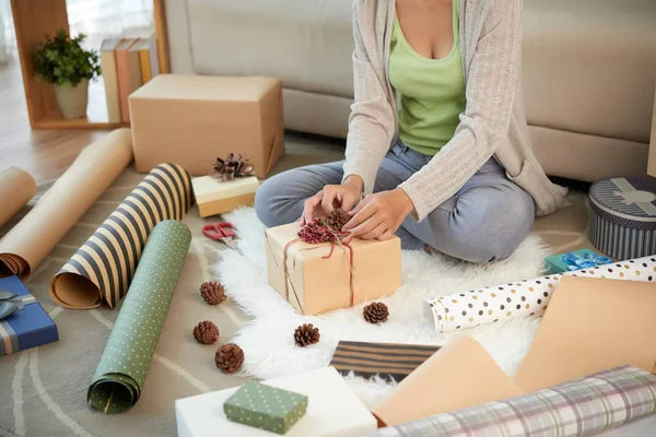 自宅で床に座って 松のコーンでクリスマスプレゼントを飾る女性の作物ショット — ストック写真