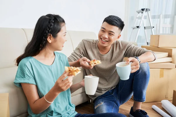 Cheerful young Asian couple enjoying pizza and drinks after moving in